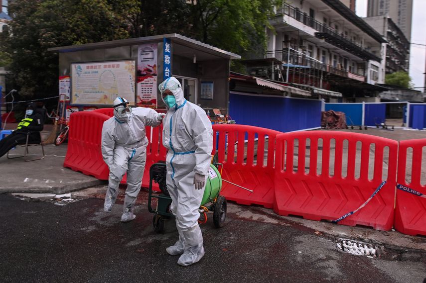 Trabajadores con traje protector caminan junto al mercado mayorista de mariscos de Huanan en Wuhan.