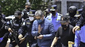 El expresidente de Honduras, Juan Orlando Hernández (centro), saluda mientras es escoltado por agentes de policía en la Dirección Nacional de Fuerzas Especiales de Honduras antes de su extradición a EE. UU.