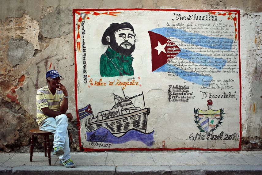 Un hombre junto a un muro con la imagen de Fidel Castro