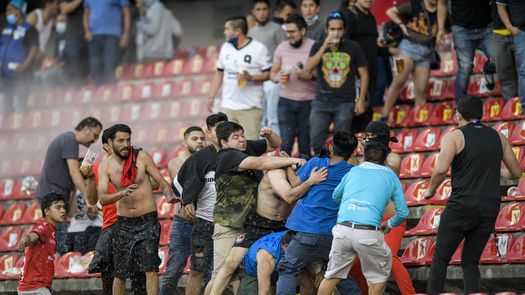 La pelea entre aficionados en la tribuna se trasladó a la cancha de fútbol, donde continuaron agrediéndose a puñetazos y patadas. Algunos utilizaron sillas, palos y barras metálicas para golpearse.
