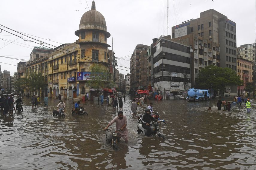 Personas cruzan una calle inundada después de fuertes lluvias monzónicas en Karachi.