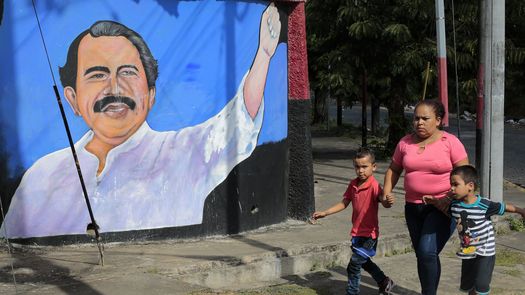 Una mujer y niños caminan junto a un mural que representa al presidente de Nicaragua, Daniel Ortega.