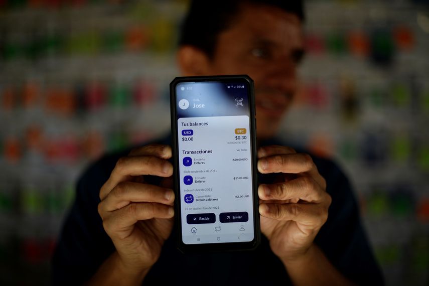 AME2900. SAN SALVADOR (EL SALVADOR), 07/12/2021.- Un hombre sostiene un teléfono que muestra la aplicación digital Chivo, para el uso y canje de criptomonedas a dólares, hoy, en San Salvador (El Salvador). El Salvador cumple este martes tres meses desde la implementación del bitcóin como moneda de pago junto al dólar estadounidense, en medio de las expectativas generadas por el anuncio de la construcción de lo que se prevé sea la primera 