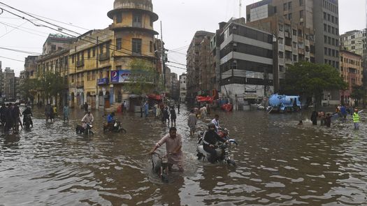 Personas cruzan una calle inundada después de fuertes lluvias monzónicas en Karachi.
