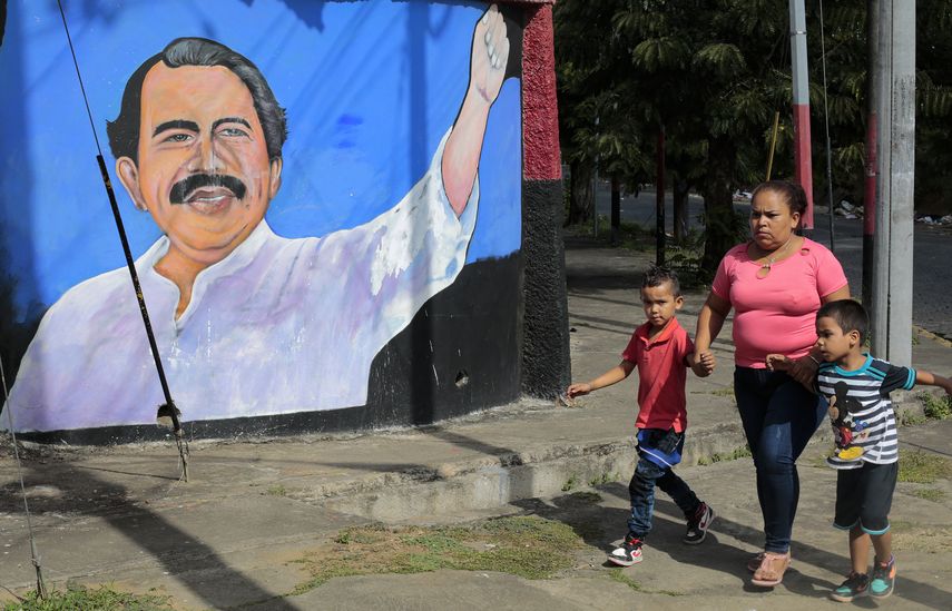 Una mujer y niños caminan junto a un mural que representa al presidente de Nicaragua