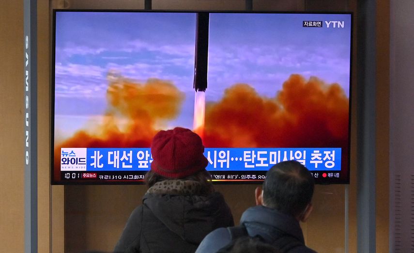 La gente mira una pantalla de televisión que muestra una transmisión de noticias con imágenes de archivo de una prueba de misiles de Corea del Norte.