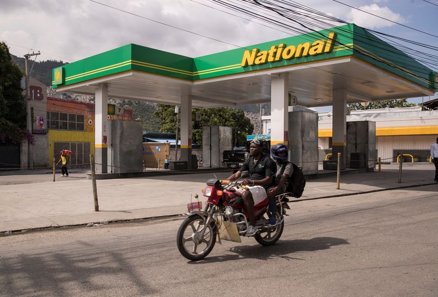Hombres en motocicleta cruzan frente a una estación de suministro de gasolina que no está prestando servicio al público.