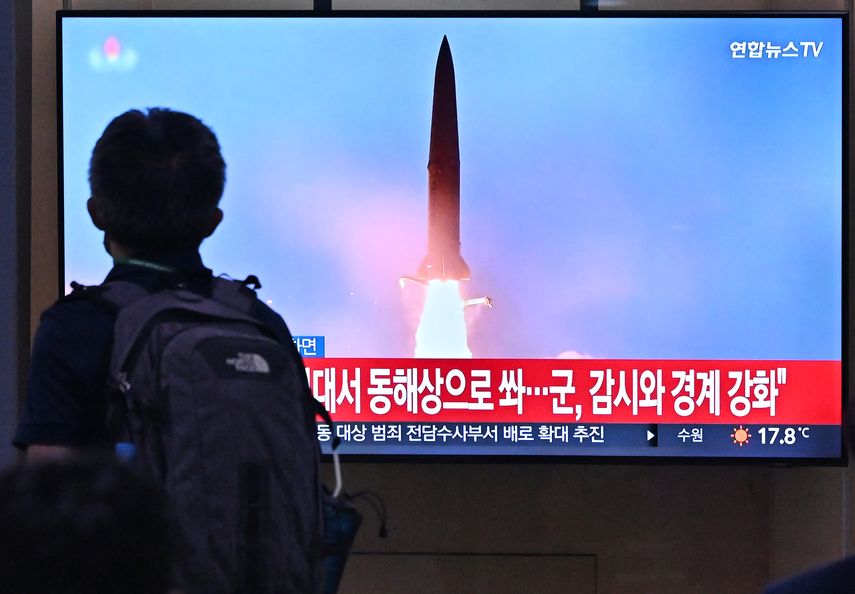 Un hombre pasa frente a una pantalla de televisión que muestra una transmisión de noticias con imágenes de archivo de una prueba de misiles de Corea del Norte.