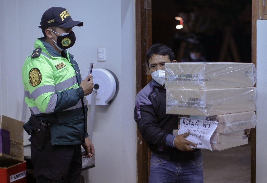 Un oficial de la Policía de Perú vigila mientras trabajadores del organismo electoral trasladan material a los centros de votación.