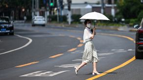 Peatón cruzando una calle mientras sostiene un paraguas para protegerse del sol en medio de temperaturas récord en China.